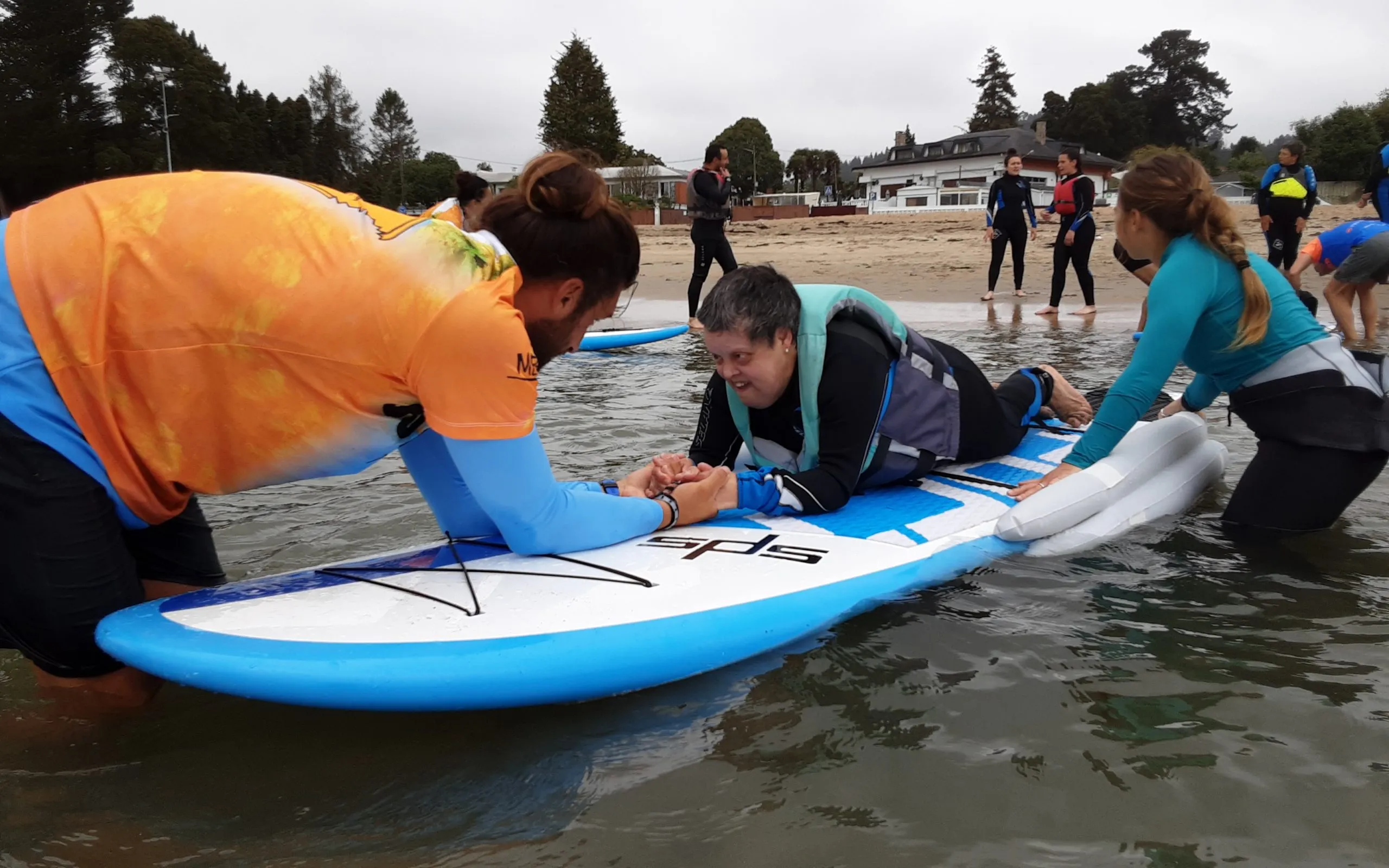 Actividade inclusiva de lecer na auga con varias persoas acompañando a unha participante sobre unha táboa.