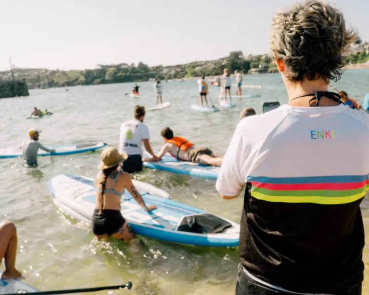 Personas de pie en aguas poco profundas con tablas de paddle surf durante una actividad de Enki.