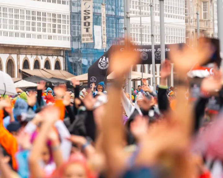 Una multitud con las manos levantadas reunida en un evento al aire libre en una plaza de la ciudad.